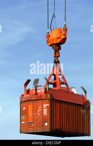 Shipping container suspended mid-air by loading crane. Cargo containers moved on industrial commercial dock. Shipping industry and commerce USA Stock Photo