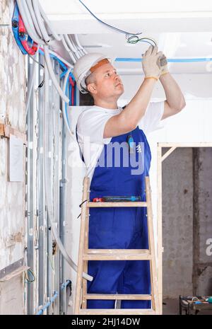 Experienced electrician laying electric wires in building under construction Stock Photo