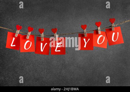 I love you on red square pieces of paper on grey background. clothespins in the form of hearts on a rope. valentine's day Stock Photo