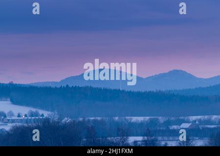 Vast upland covered with a thin layer of snow. Distant dark hills. Over the peaks a partly cloudy red sky, tinged with the light of the setting sun. Stock Photo