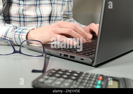 Office worker in checked shirt working at laptop with glasses and calculator on desk Stock Photo