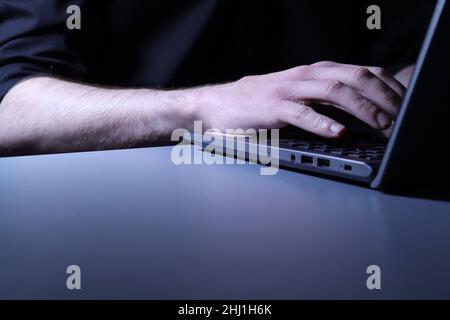 Sinister looking individual in black shirt typing at laptop Stock Photo