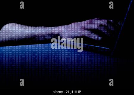 Hacked (DARK) - Hands at computer with binary code overlay with the word 'HACKED' at centre of image Stock Photo