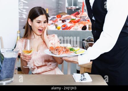 Young woman visiting fish restaurant pleasantly surprised by bringed dish Stock Photo