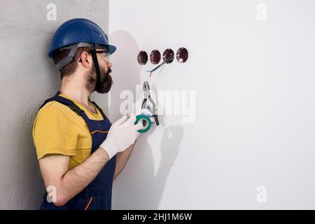 electrician in helmet installs sockets Stock Photo