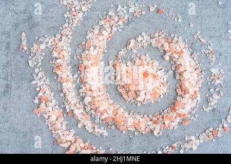 Himalayan salt scattered in a spiral shape on a gray background, top view Stock Photo