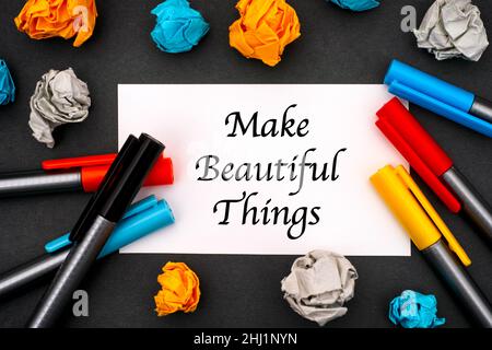 White paper with words Make Beautiful Things, colour pens and crumpled paper on a black background. Stock Photo