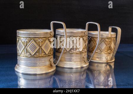 A metal cup holder on a blue table with a reflection. Kitchen utensils on a black background Stock Photo
