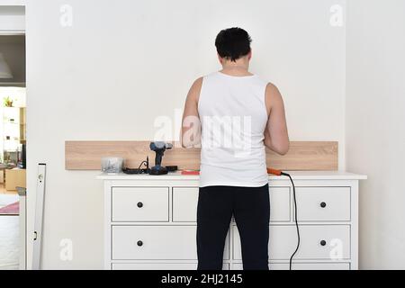 Man mounting shelves on the wall. All necessary tools are placed on the chest of drawers Stock Photo
