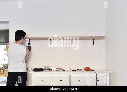 Man mounting shelves on the wall. All necessary tools are placed on the chest of drawers Stock Photo