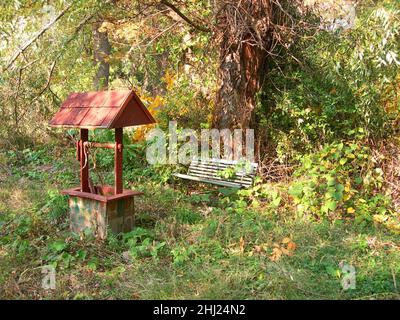 Red wooden Wishing Well & bench in the woods in the fall at sunset.