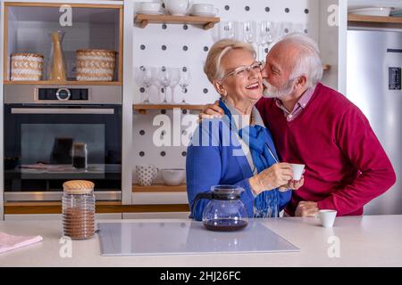 Happy senior couple having their coffee in the kitchen. Husband congratulates his wife on Valentine's day or their wedding anniversary. Stock Photo