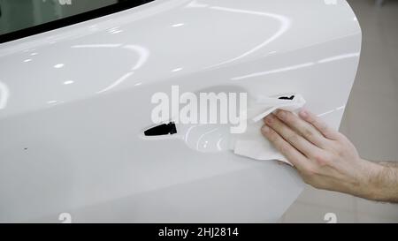 A worker wipes the film on a car with a paper napkin. Car detailing. Worker sticking protective transparent film on a car body in place of the door ha Stock Photo