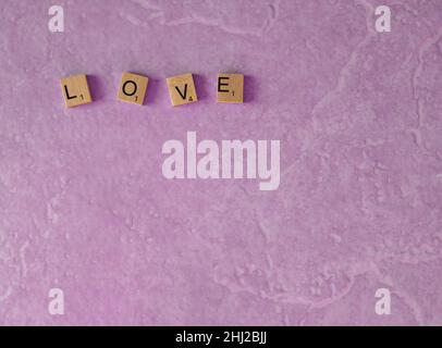 the word love spelt out in wooden squares on a light pink background shot from above copy space Stock Photo