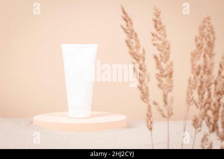 Blank plastic cosmetics tube on round platform podium on white sand background. Skincare, moisturizer, face, body, hand cream, shampoo package Stock Photo