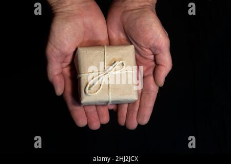 Small box with a gift in hands on a black background. Stock Photo