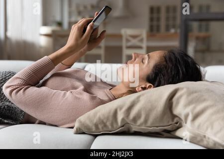 Serene woman relaxing lying on cushion on sofa with smartphone Stock Photo