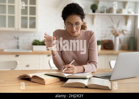 Serious young Latina woman studying seated at dining table Stock Photo