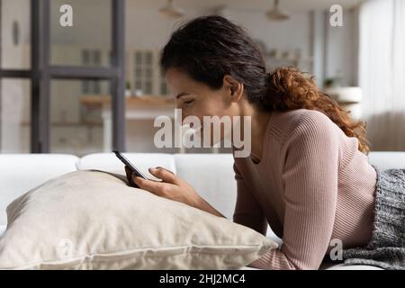 30s attractive woman lying on comfy sofa using smartphone Stock Photo