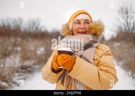 Woman in yellow winter clothes holds hot coffee or tea drink from paper cup outdoors in winter park
