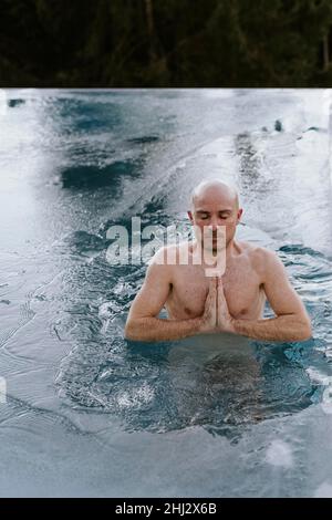 Man ice bathing in the pool folds his hands and meditates Stock Photo