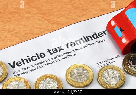 Top of a vehicle tax reminder letter with one pound coins anda model car. No people. Cost of running a car concept. Stock Photo
