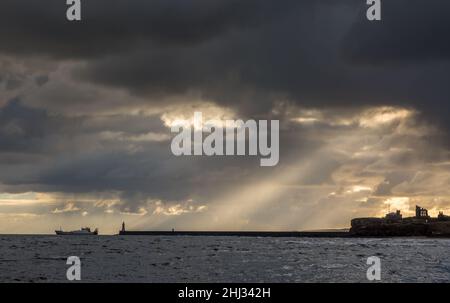 Crepuscular rays shine down on Tynemouth, the Priory & the pier in the northeast of England on a cloudy day Stock Photo