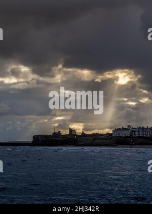 Crepuscular rays shine down on Tynemouth, the Priory & the pier in the northeast of England on a cloudy day Stock Photo