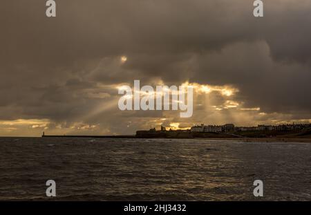 Crepuscular rays shine down on Tynemouth, the Priory & the pier in the northeast of England on a cloudy day Stock Photo