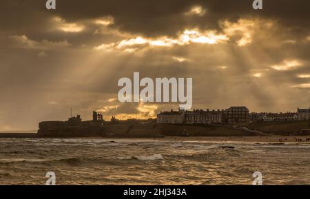 Crepuscular rays shine down on Tynemouth, the Priory & the pier in the northeast of England on a cloudy day Stock Photo