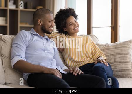 Dreamy couple sit on sofa daydreaming looking into distance Stock Photo