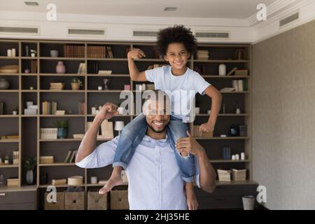 Little son sits on strong fathers shoulders demonstrate biceps strength Stock Photo