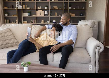 African spouses relaxing on couch in living room using tablet Stock Photo