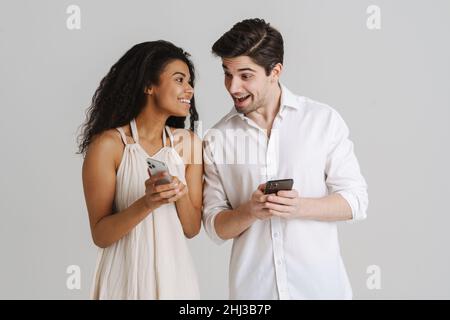 Young multiracial couple smiling while using mobile phones isolated over white background Stock Photo