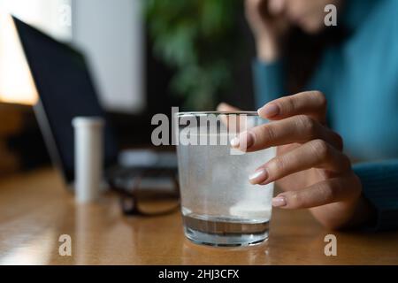 Woman feel sick in office wait for pill tablet dissolving in water glass. Ill female take medication Stock Photo