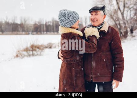 Portrait of senior family couple walking outdoors during snowy winter weather. Mature people hugging wearing warm clothes. Valentine's day Stock Photo