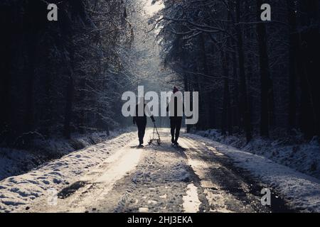 Couple of people with small child walking on sunny road in forest Stock Photo
