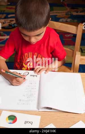 Education Preschool boy at table writing words that begin with the letter B in his notebook Stock Photo