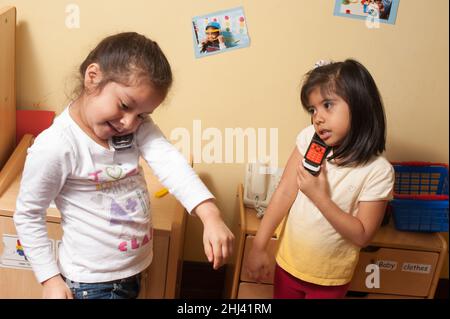 Education Preschool 4-5 year olds two girls pretend play having simutaneous telephone converstations standing side by side in kitchen family area Stock Photo