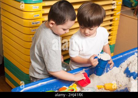 Education Preschool 4-5 year olds two boys playing together at sand table Stock Photo