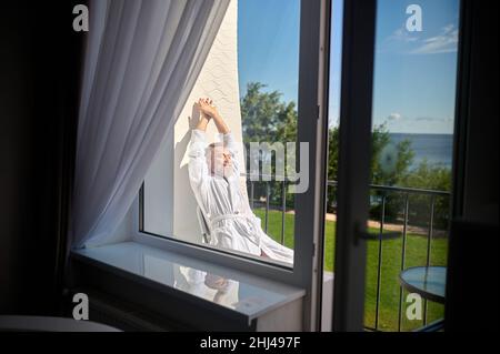 Holidaymaker in the white bathrobe basking in the sunlight Stock Photo