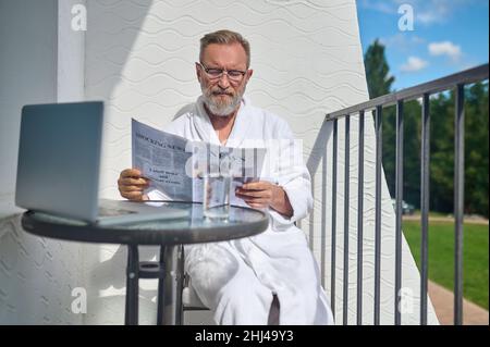 Concentrated male dressed in the white bathrobe reading news Stock Photo