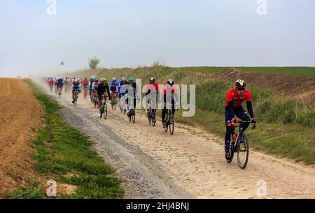 Viesly, France - April 14, 2019: The peloton riding on the dusty cobblestone road from Briastre to Viesly during Paris Roubaix 2019. Stock Photo