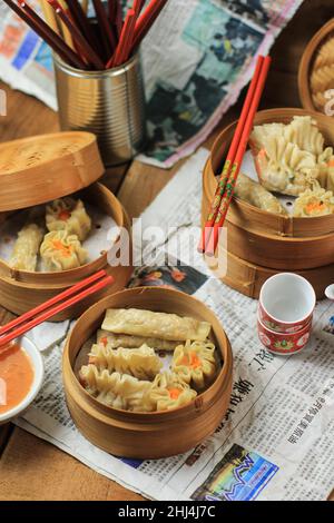 Bandung, Indonesia, 02122018: Shrimp Chinese/Korean Steamed Dumpling (Dim Sum or Shumai) with Sauce, on Bamboo Steamer with Chinese News Paper Decorat Stock Photo