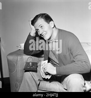 American singer Pat Boone in the UK for a series of television and variety engagements. 22 year old Pat is a father of three children. He has sold 14,000,000 records in two years. He is still studying for his BA and works about two weeks a month singing and two weeks at college. Pictured, he is busy working out the English money which is baffling him. Although he earns big money, he likes to spend his money wisely. 25th December 1956. Stock Photo