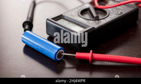 battery with volt calculator, voltmeter, multimeter red positive pole, black negative pole, on wood work table Stock Photo