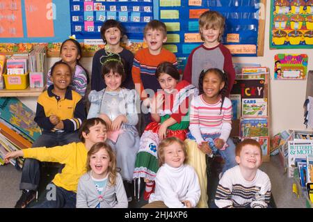 Group of Kindergarten students posing in classroom, two girls wearing dressup clothes Stock Photo