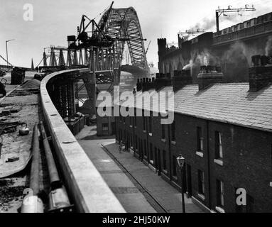 An unusual view of the Widnes-Runcorn Bridge, now almost completed, showing how the approach road soars above the rows of terraced houses in Widnes. On the right is the rail way crossing. 8th June 1961.