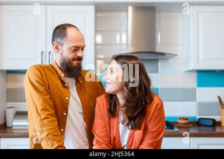 Happy young couple talking at home in kitchen. Family Husband and wife enjoying spending time together while standing in apartment interior. family Stock Photo