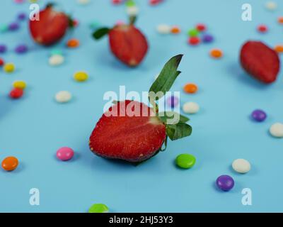 sliced fresh strawberries and colorful sweet candy on blue background. concept Stock Photo
